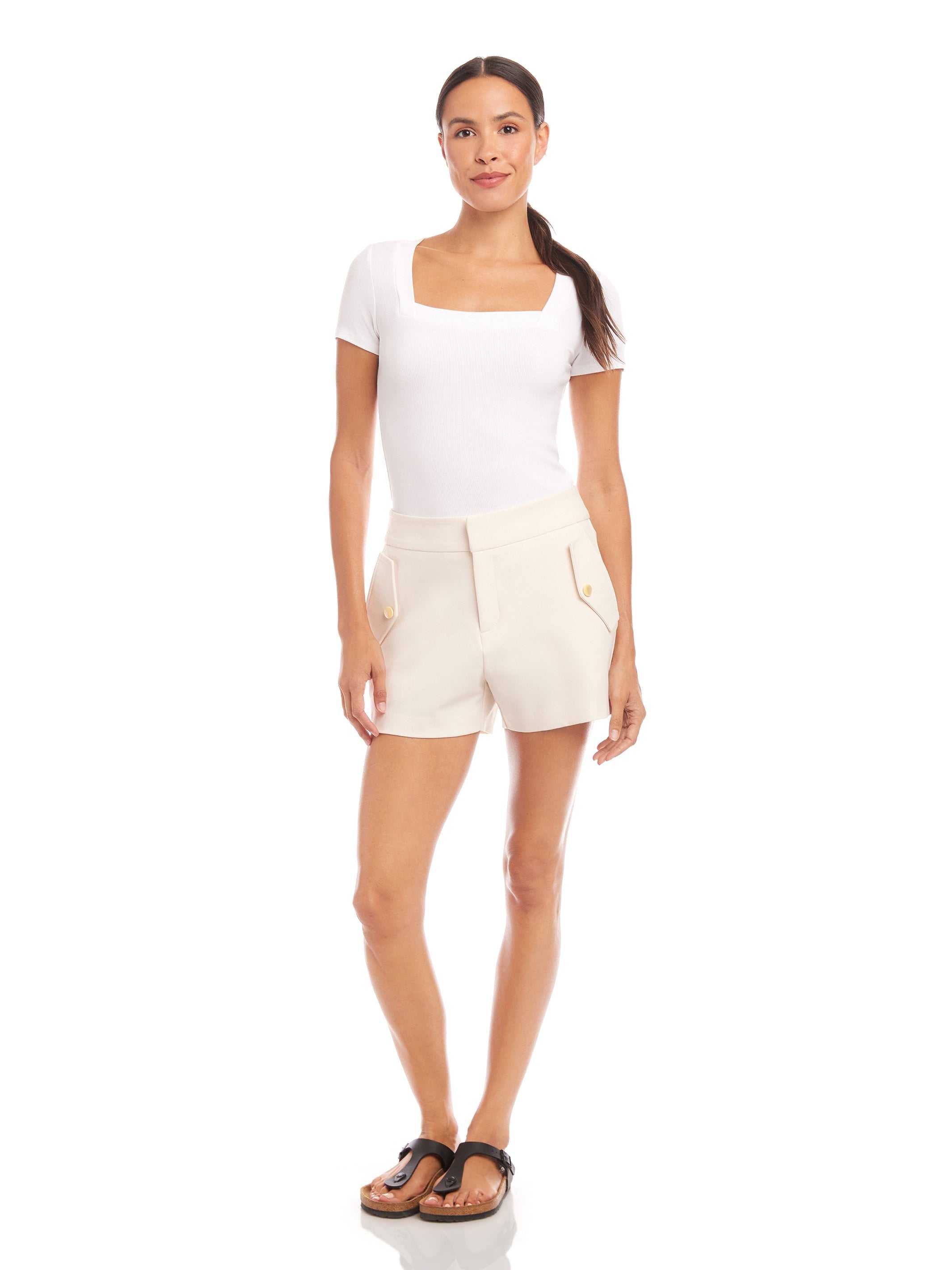 Woman wearing ecru Alma shorts with stretch fabric, side pockets, and pearl buttons, styled with a white top and sandals.