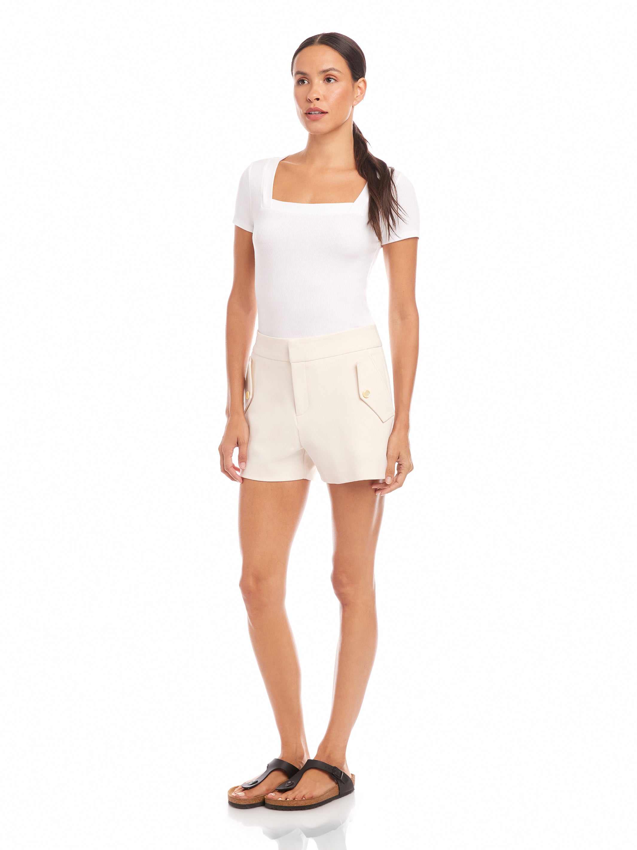 Woman wearing ecru Alma shorts with side pockets and pearl button details, paired with a white fitted top and sandals.
