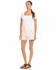 Woman wearing ecru Alma shorts with side pockets and pearl button details, paired with a white fitted top and sandals.