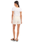 Woman wearing ecru Alma shorts with relaxed fit and side pockets, paired with white t-shirt and sandals, back view