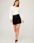 Woman wearing black Cece pleated trouser shorts with a white long-sleeve button-up blouse and black sandals.