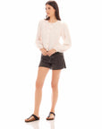 Woman wearing Aubrey button-up blouse with long bishop sleeves and front buttons paired with black shorts and sandals