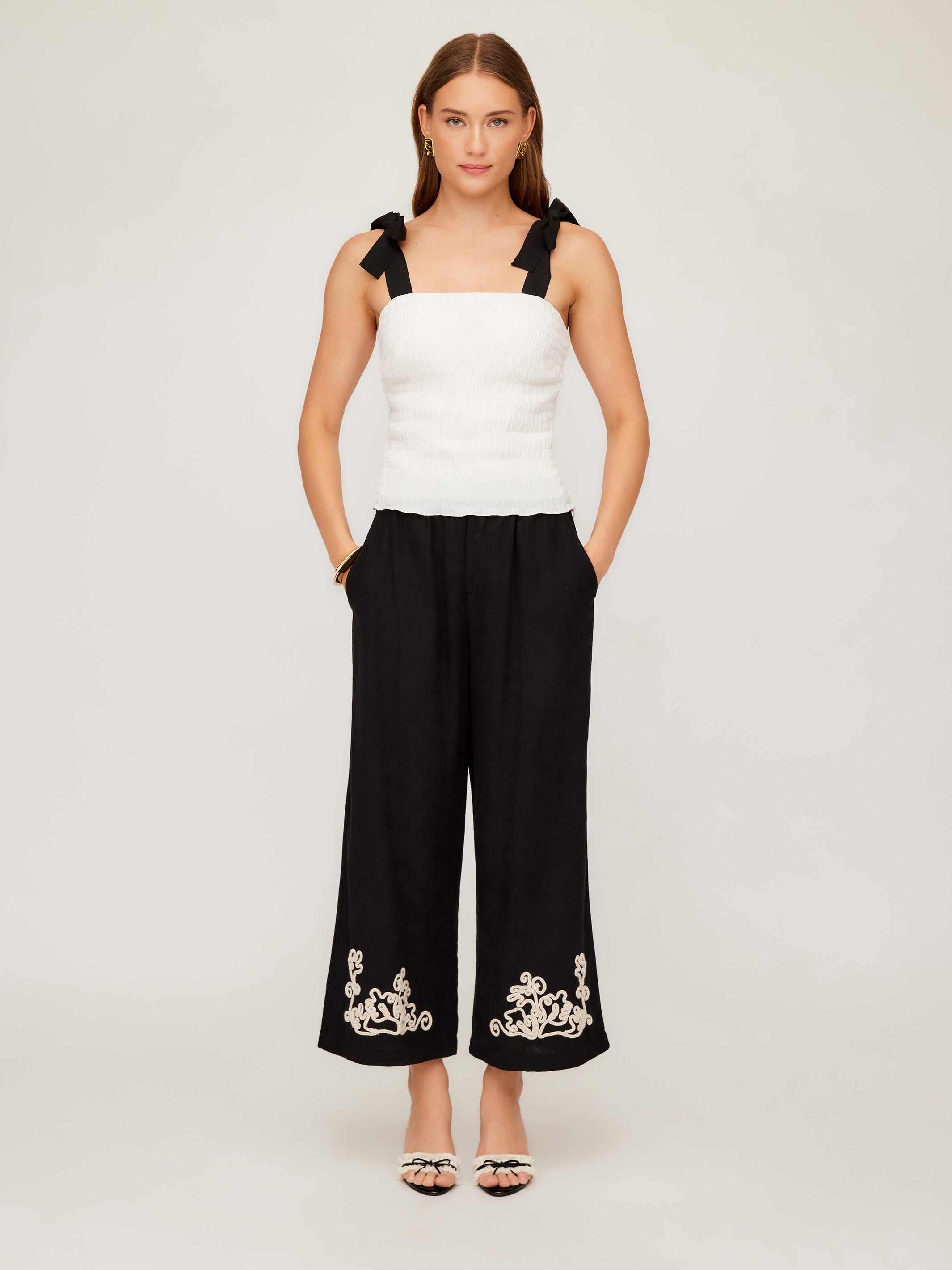 Woman wearing Annie Ribbon Tie Top white sleeveless square neck fitted linen blouse with black wide-leg pants and sandals