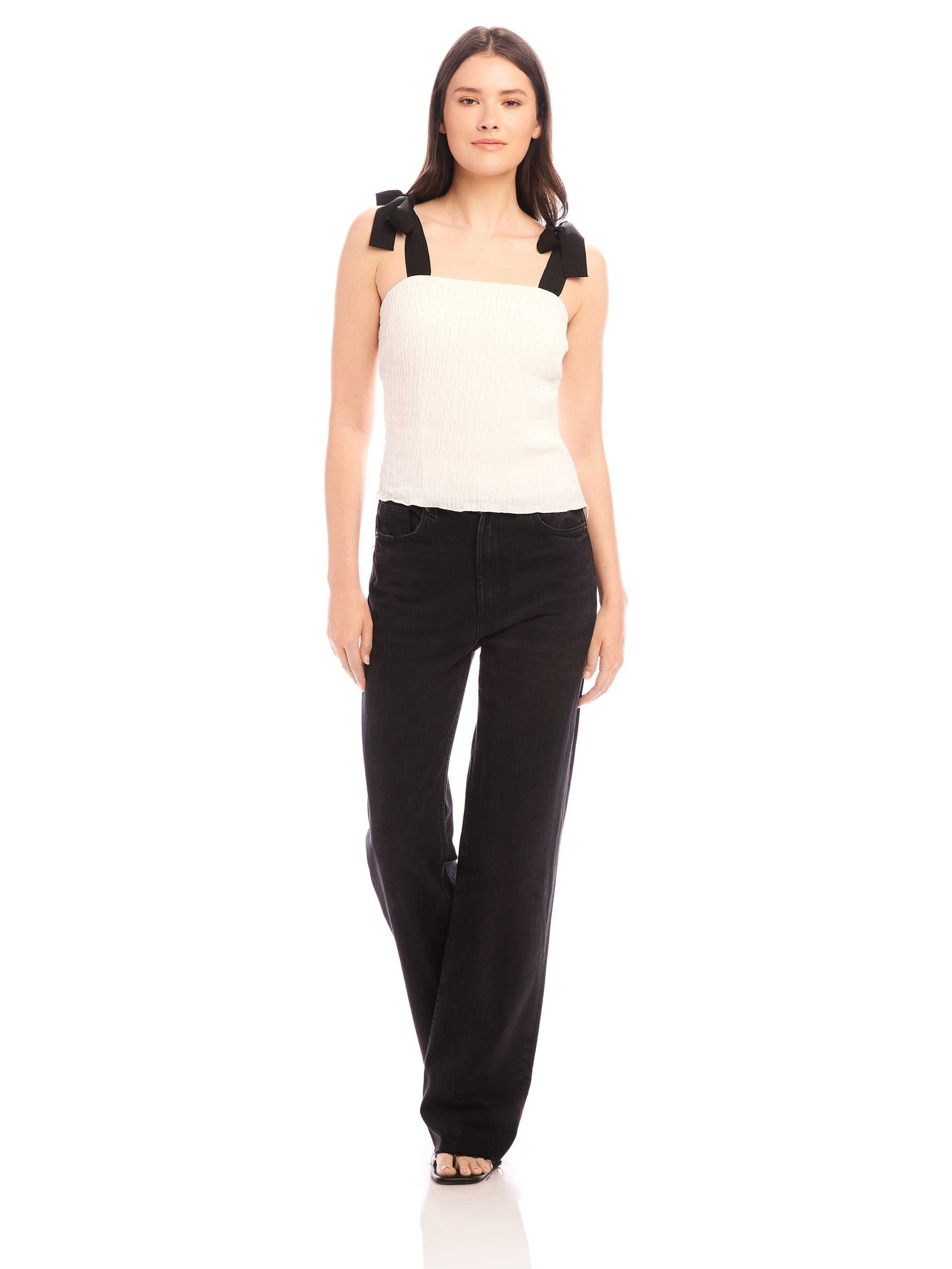 Woman wearing Annie Ribbon Tie Top white sleeveless square neck blouse with black ribbon straps and black pants