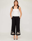 Woman wearing Annie Ribbon Tie Top white sleeveless square neck fitted linen blouse with black wide-leg pants and sandals