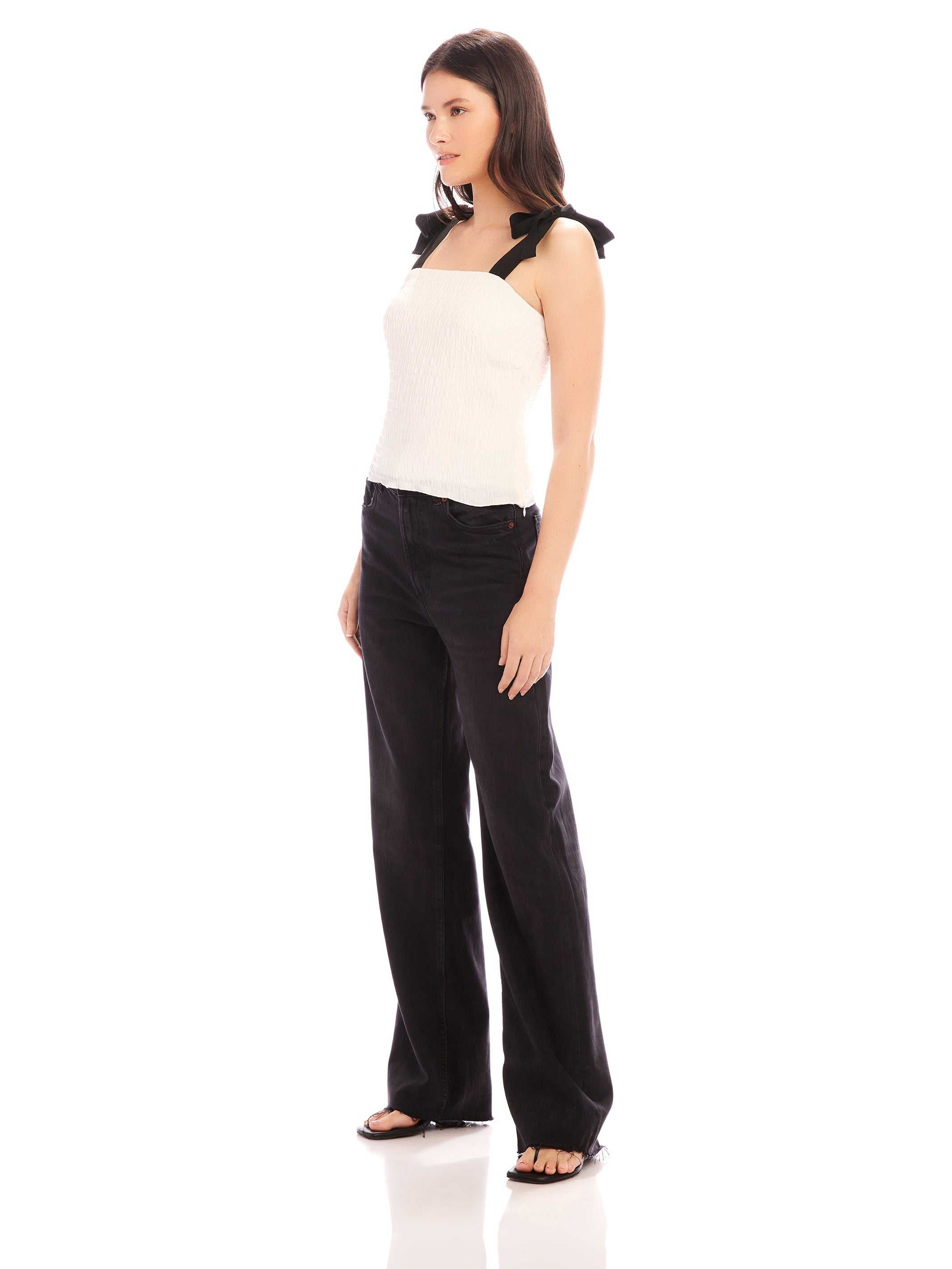 Woman wearing sleeveless fitted Annie Ribbon Tie Top with square neck and black ribbon straps paired with black pants.