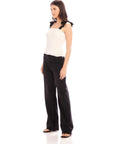 Woman wearing sleeveless fitted Annie Ribbon Tie Top with square neck and black ribbon straps paired with black pants.