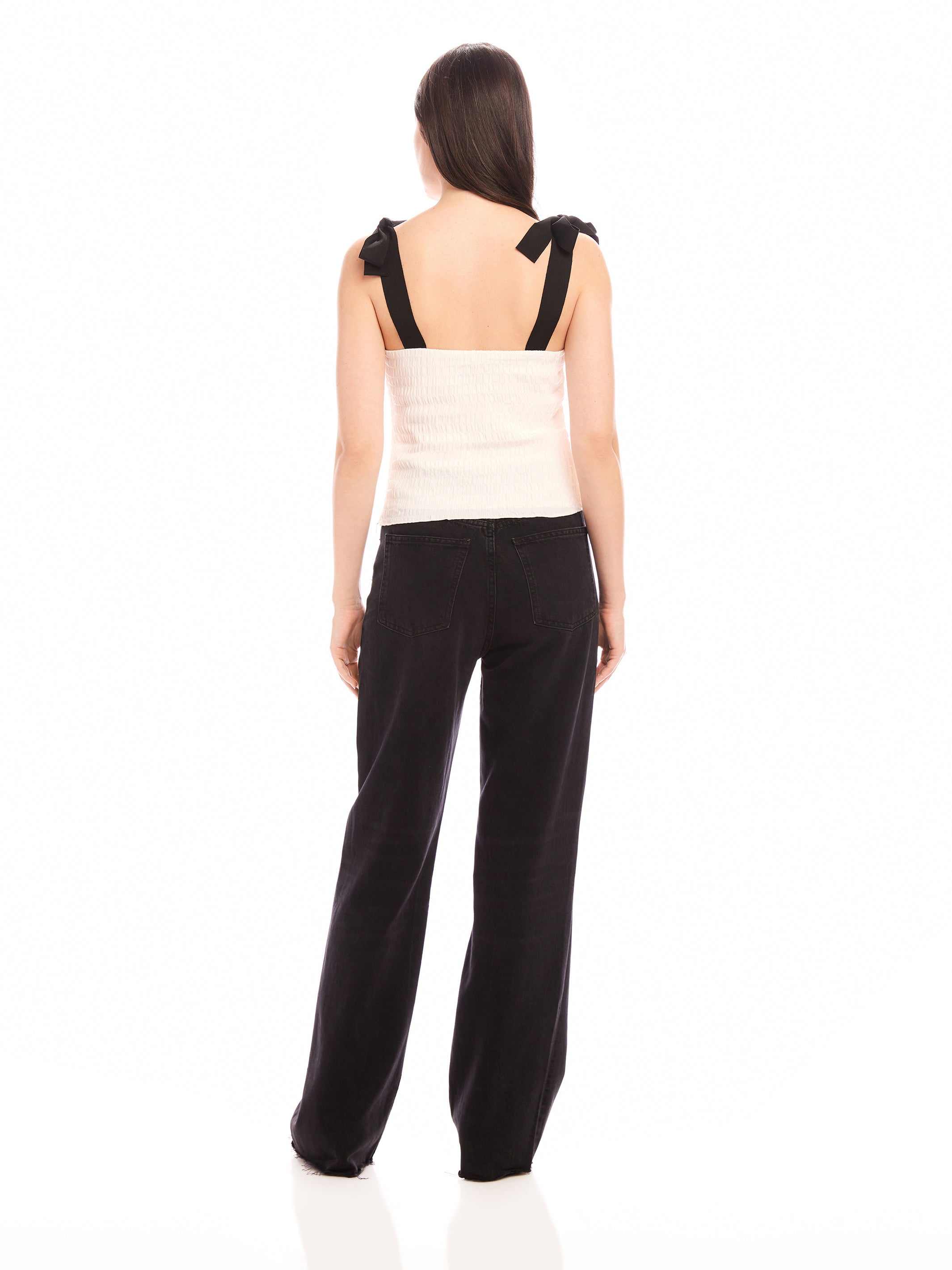 Back view of woman wearing Annie Ribbon Tie Top with black adjustable tie straps, square neck, paired with black wide-leg pants