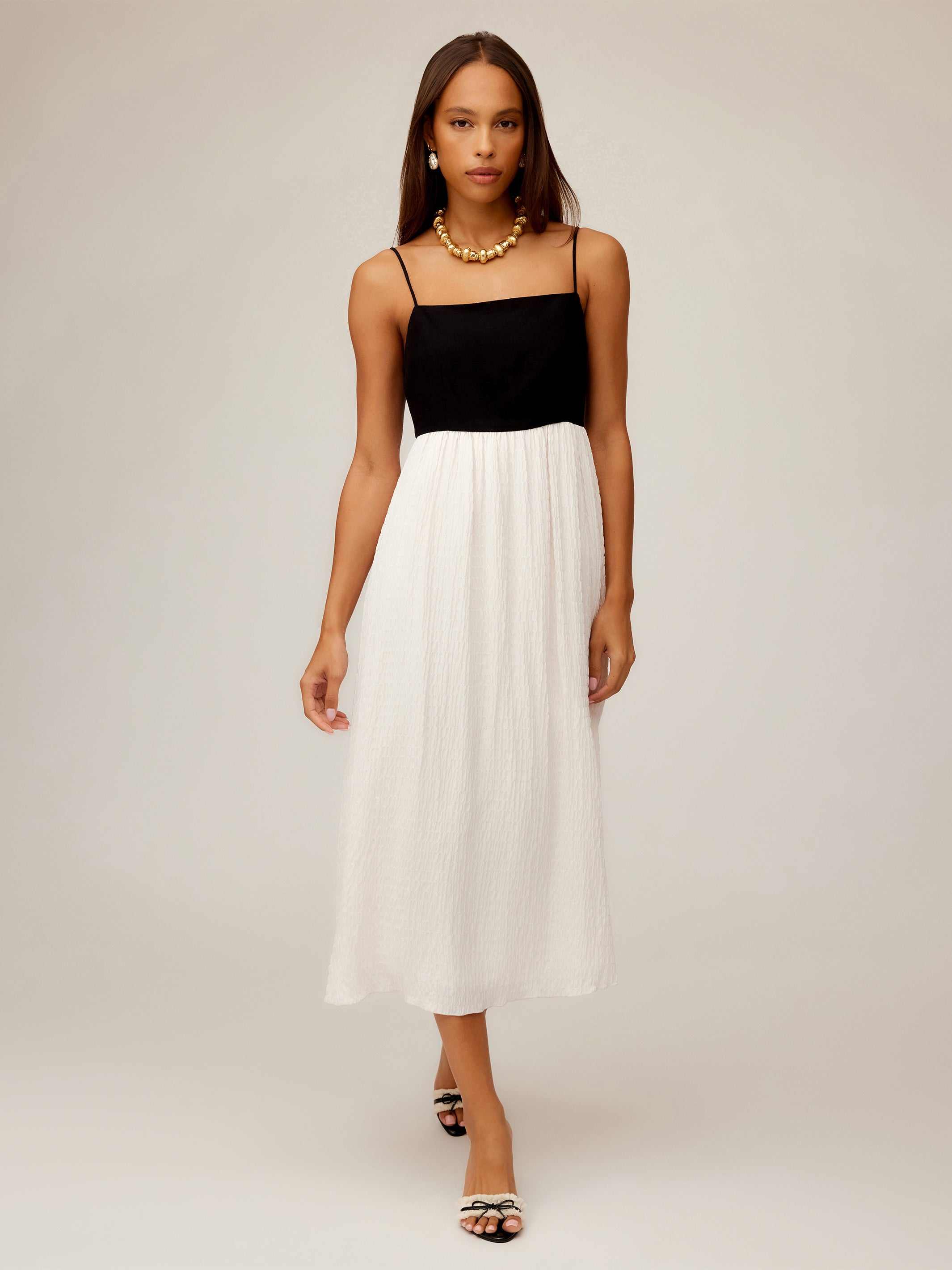 Woman wearing Anetta Contrast Midi Dress with fitted black top and flowy white skirt, featuring adjustable spaghetti straps and square neckline.