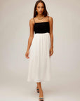 Woman wearing Anetta Contrast Midi Dress with fitted black top and flowy white skirt, featuring adjustable spaghetti straps and square neckline.
