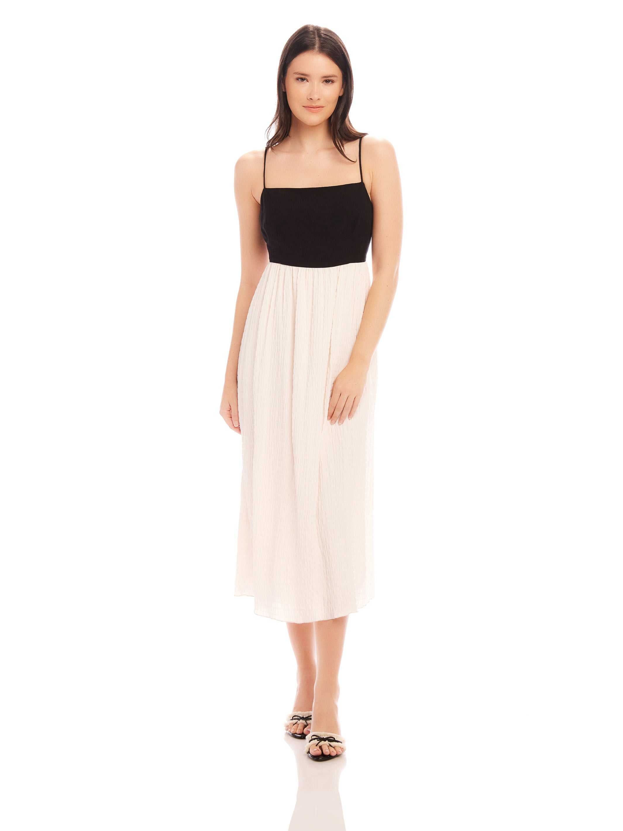 Woman wearing Anetta Contrast Midi Dress with black fitted top and white flowy skirt, adjustable spaghetti straps, and square neckline.