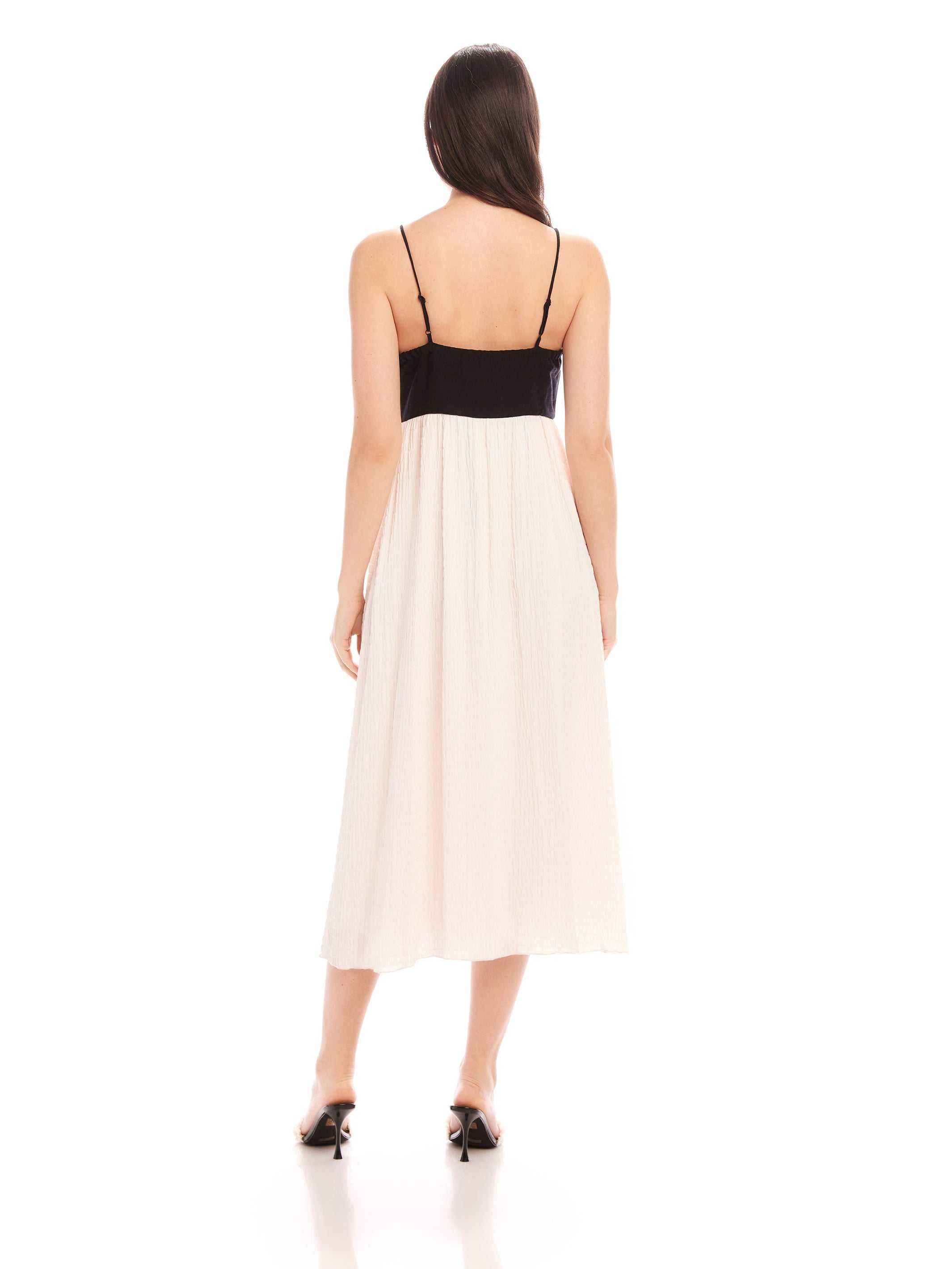 Back view of woman wearing Anetta Contrast Midi Dress with black fitted top and flowy white skirt, adjustable spaghetti straps, and midi length.