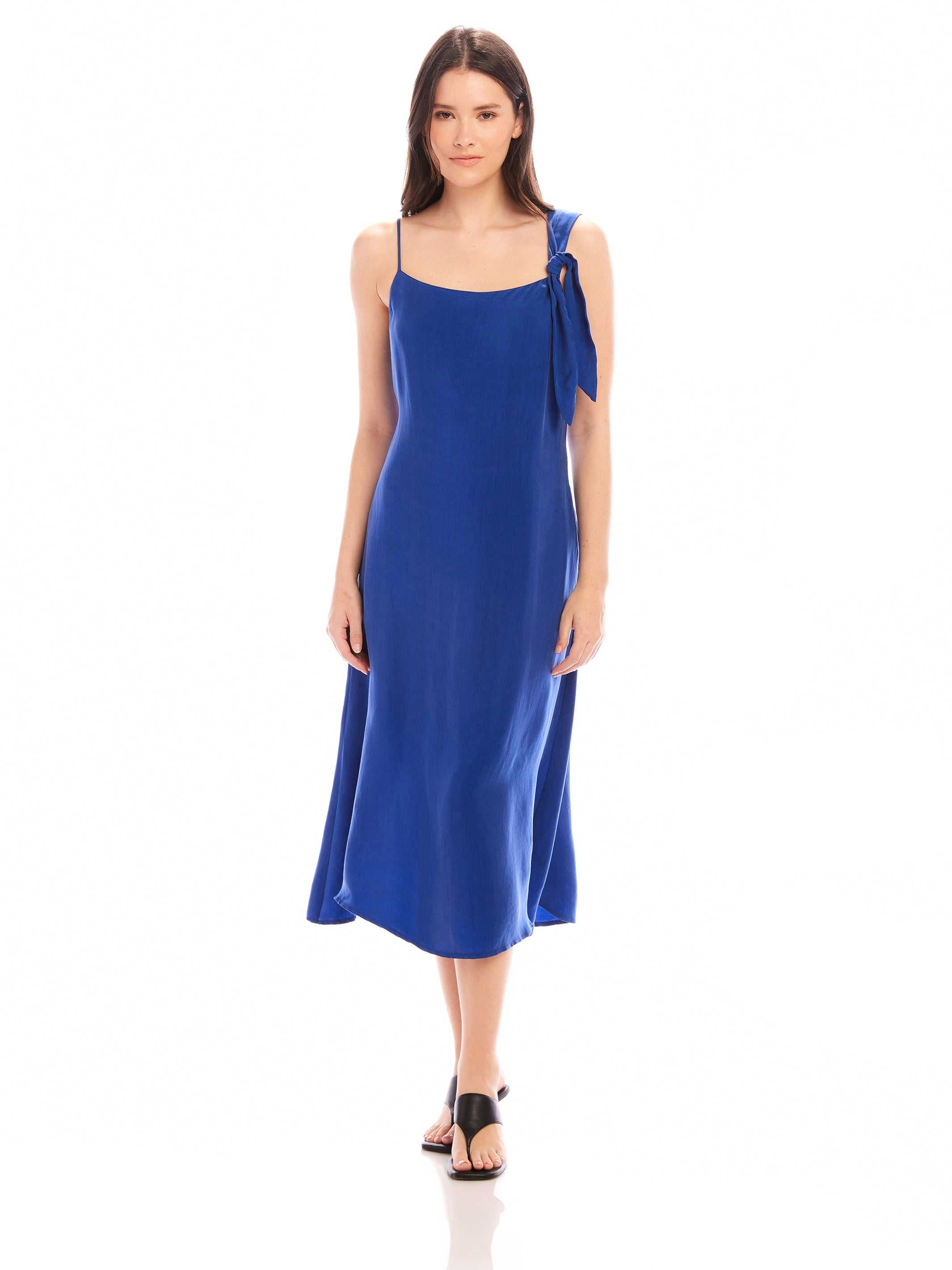 Woman wearing blue Serena Midi Dress with asymmetrical tie shoulder and scoop neck, midi length sheath style