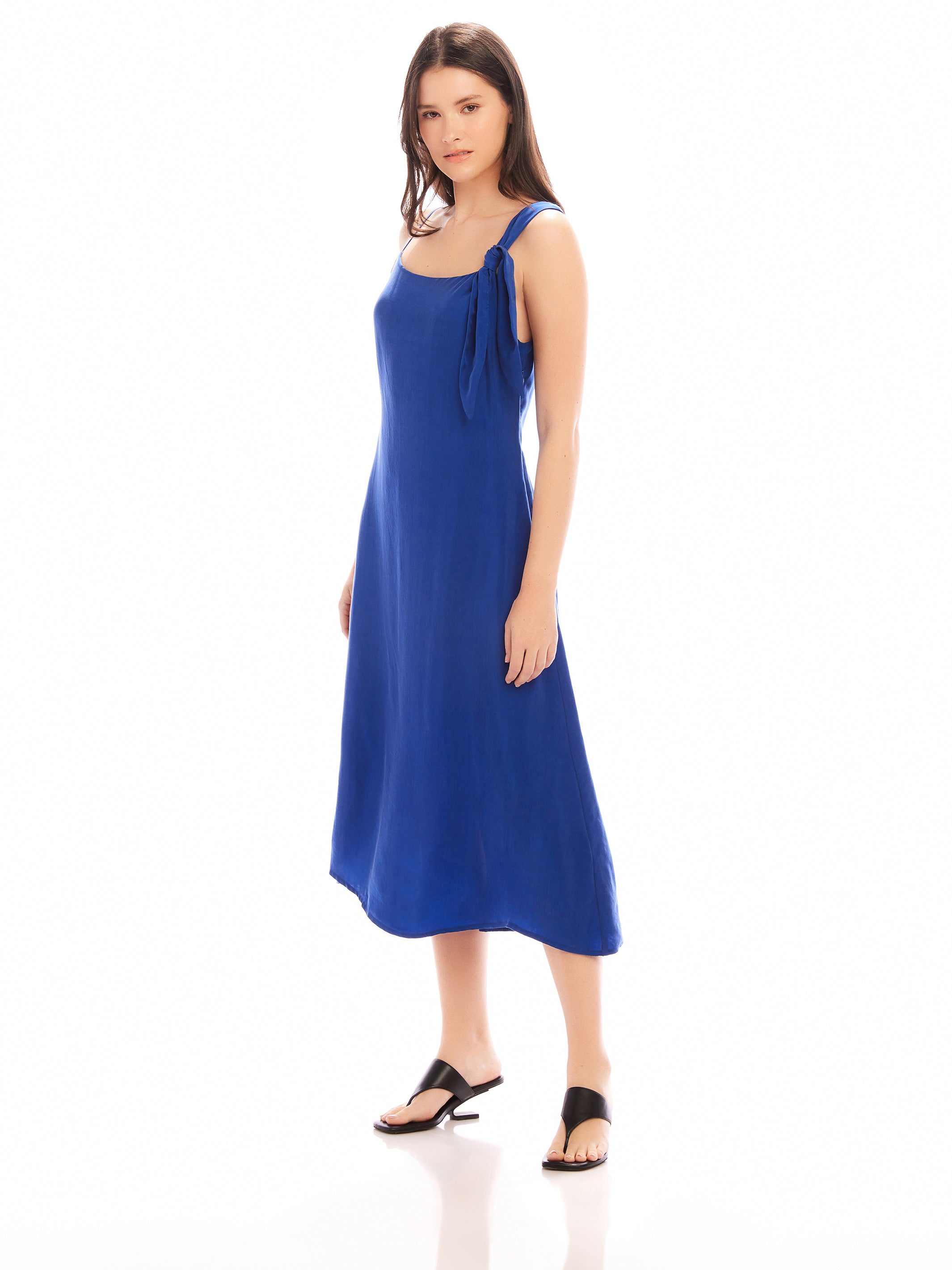 Woman wearing blue Serena Midi Dress with asymmetrical tie shoulder and scoop neck in a sheath silhouette