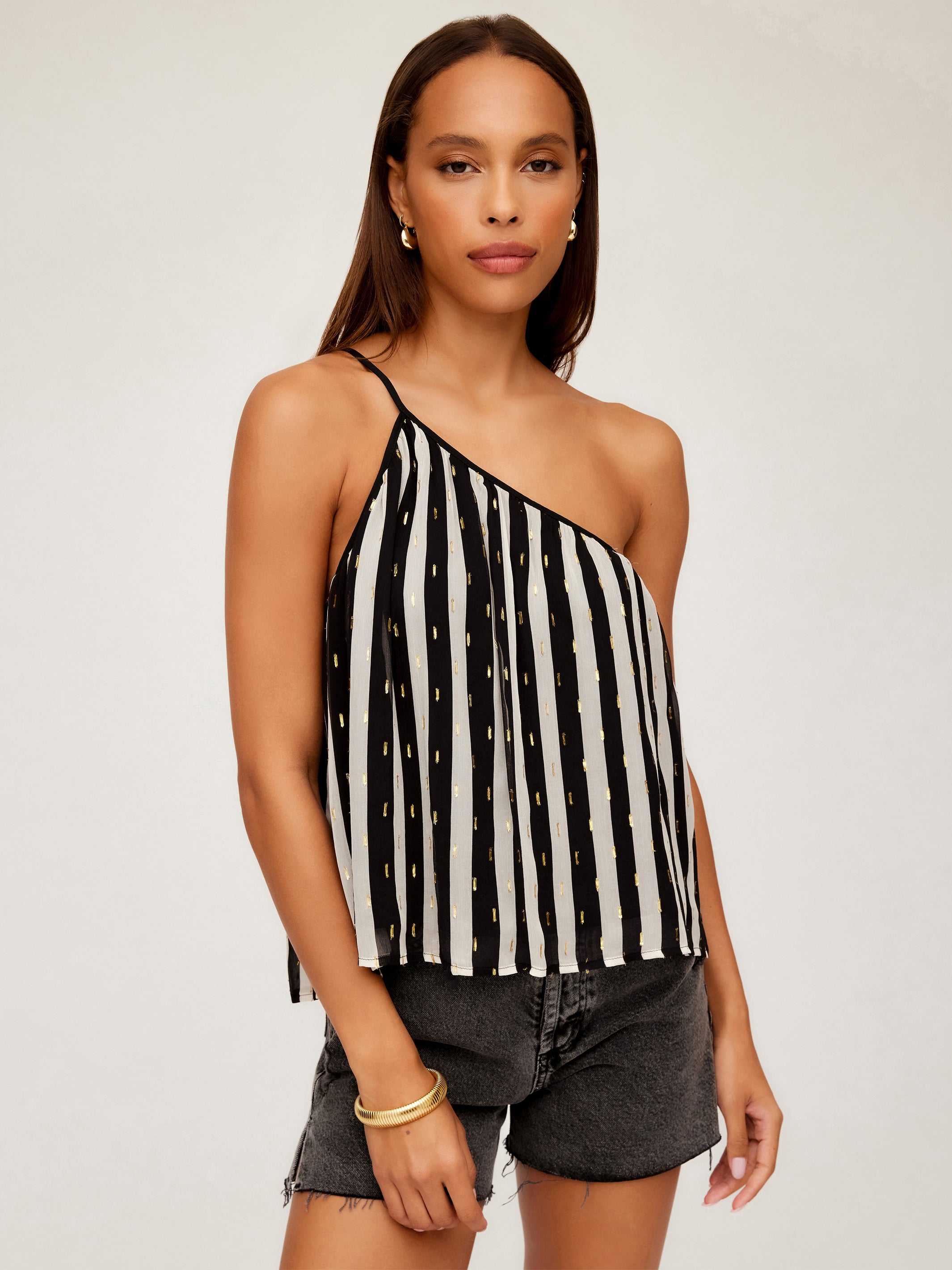 Woman wearing Louetta One-Shoulder Tank with black and white stripes and gold metallic details paired with black shorts