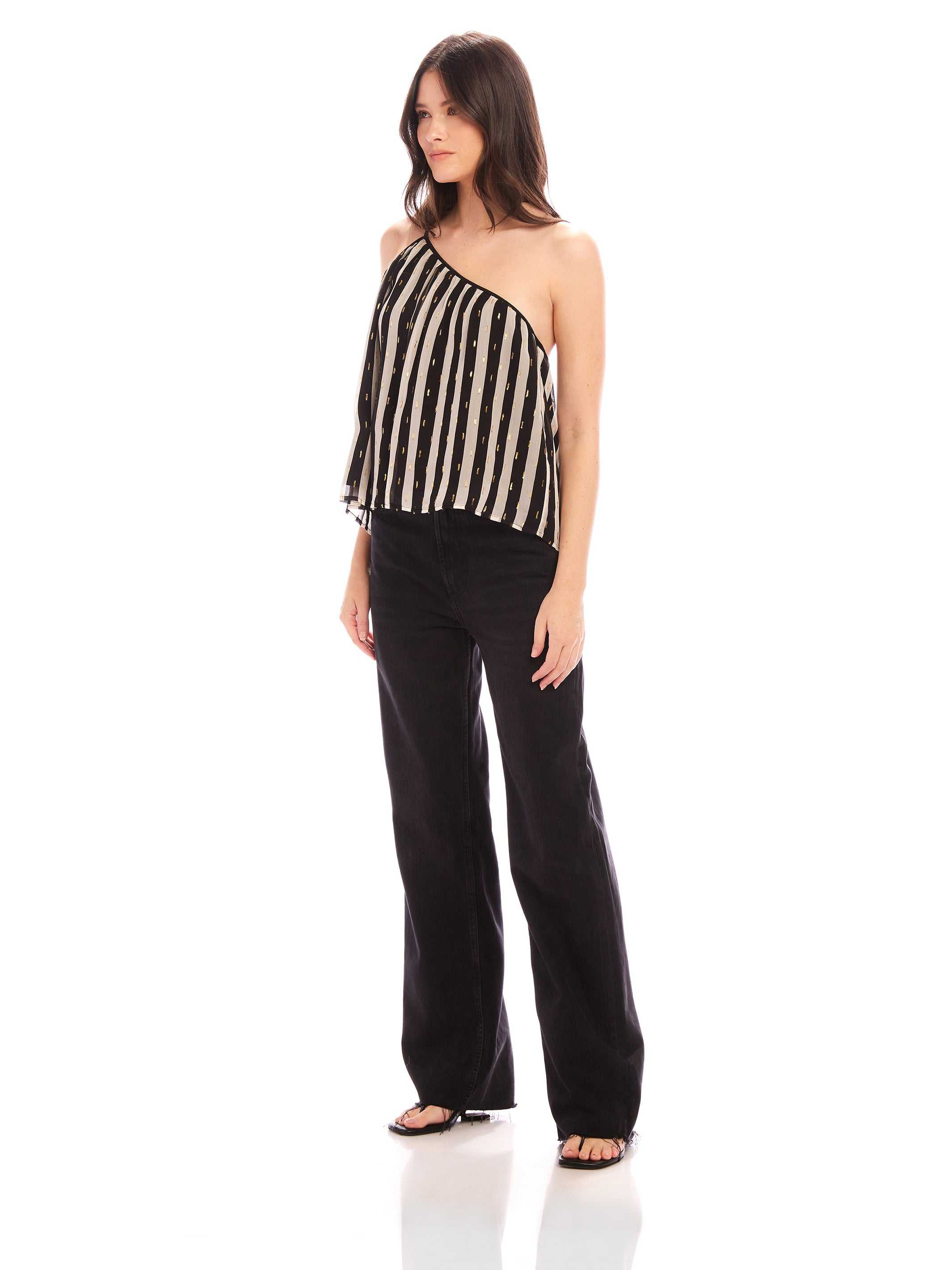 Woman wearing Louetta one-shoulder tank with black and white stripes and metallic gold foil detail paired with black pants