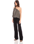 Woman wearing Louetta one-shoulder tank with black and white stripes and metallic gold foil detail paired with black pants