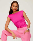 Woman wearing vibrant pink Tasha Side-Shirred Top with cap sleeves and boatneck paired with light pink pants.