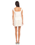Woman wearing a white Tasha Side-Shirred Top with cap sleeves and open back paired with a light skirt, back view.