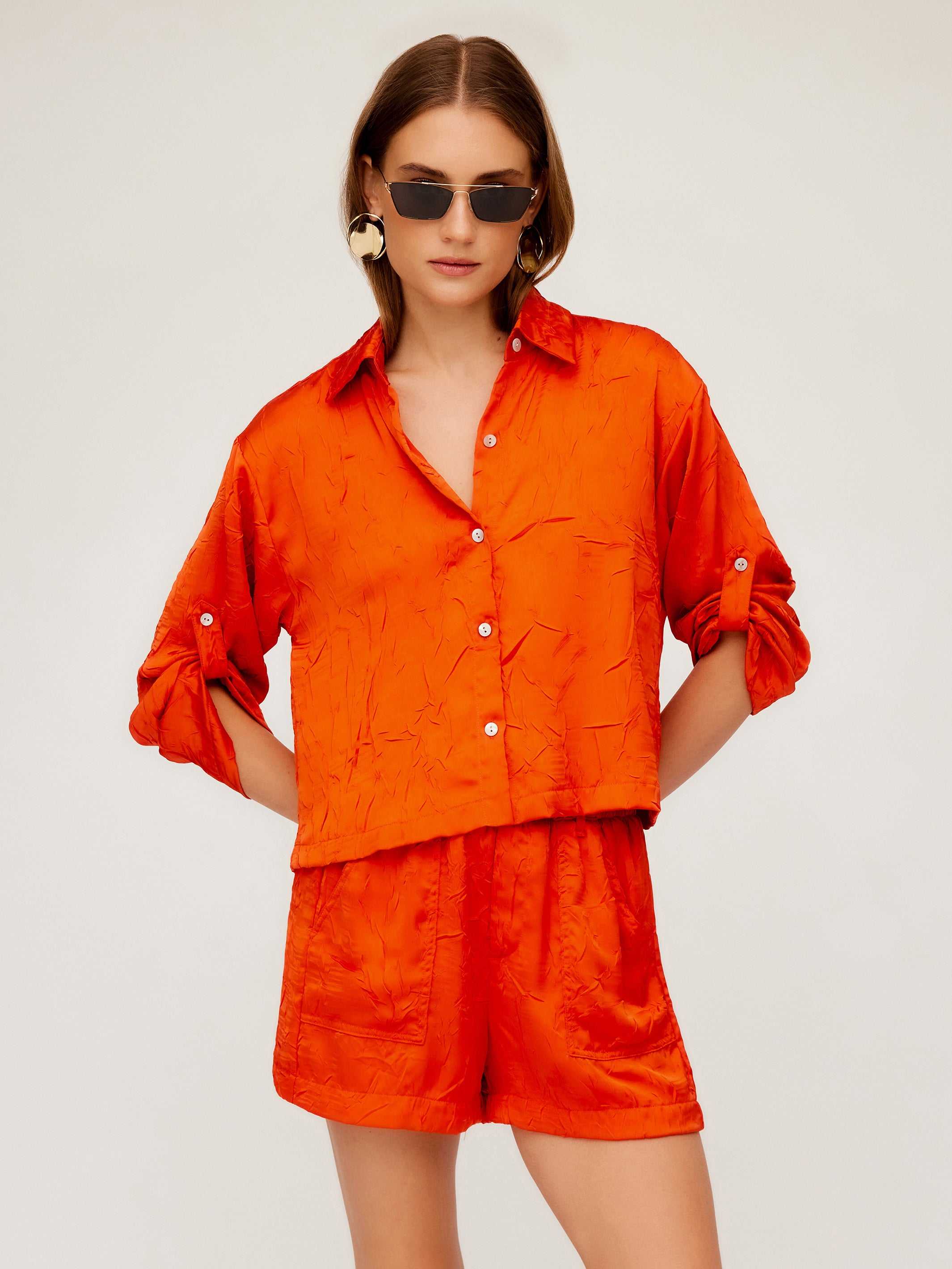 Woman wearing orange textured crushed satin Becca Shorts with matching button-up shirt and sunglasses