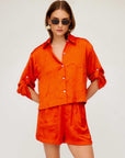 Woman wearing orange textured crushed satin Becca Shorts with matching button-up shirt and sunglasses