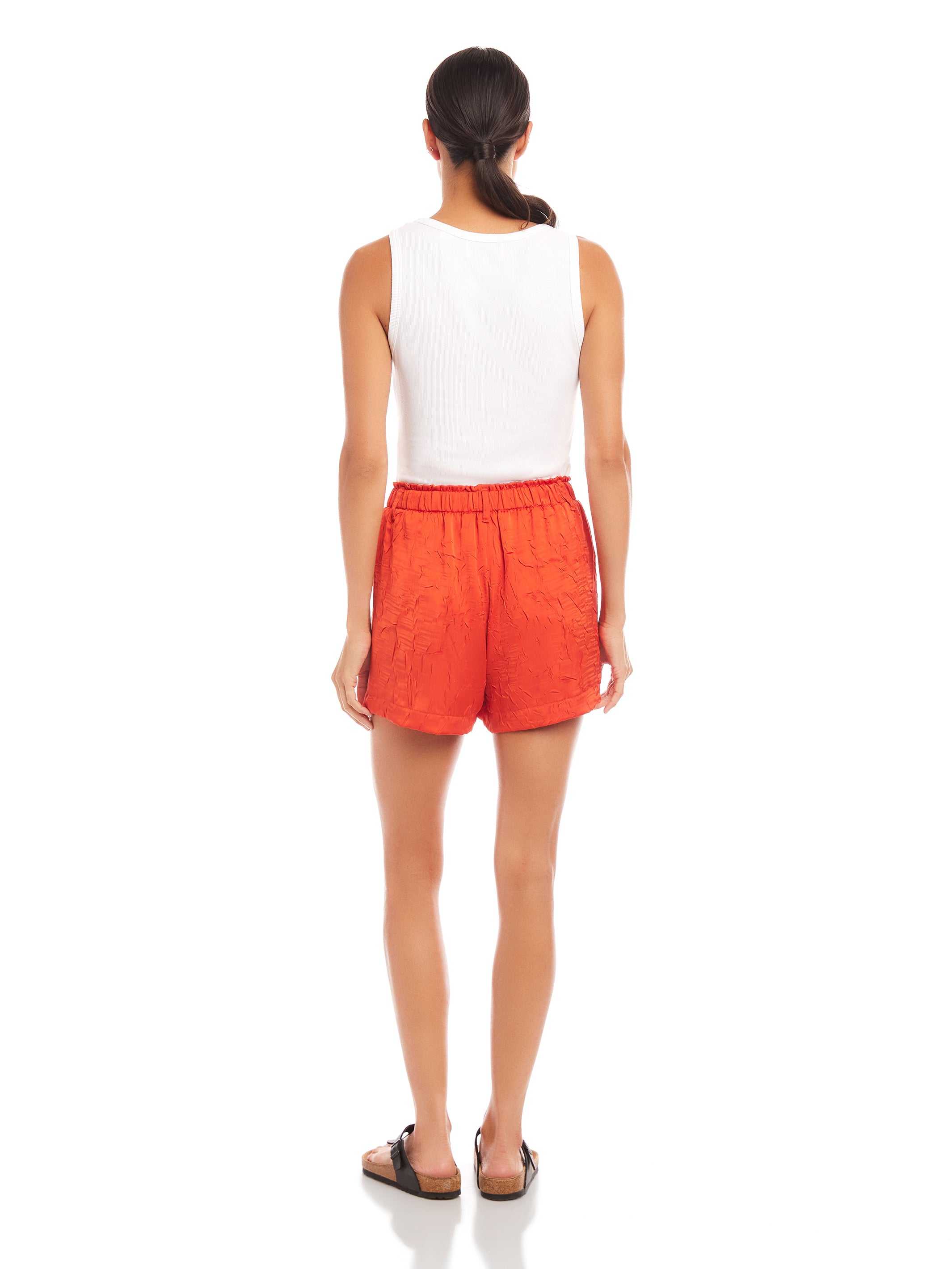 Woman wearing orange high-waist Becca Shorts with elasticized waist and front patch pockets, back view