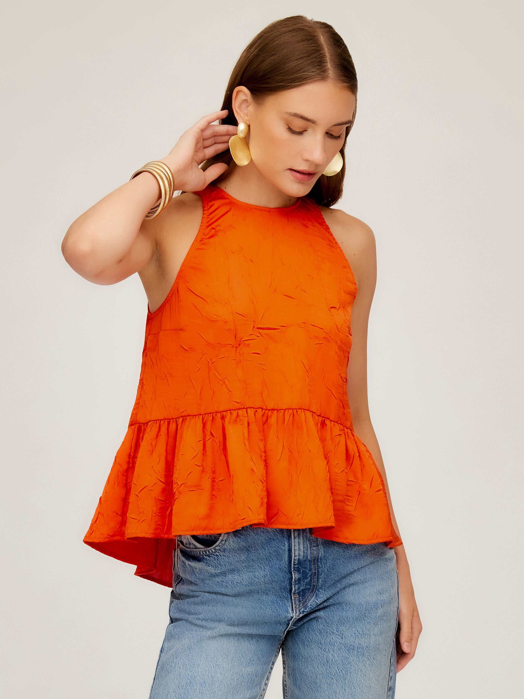 Woman wearing orange Floren Ruffle Hem crushed satin halter top with high-low hem and back tie closure.