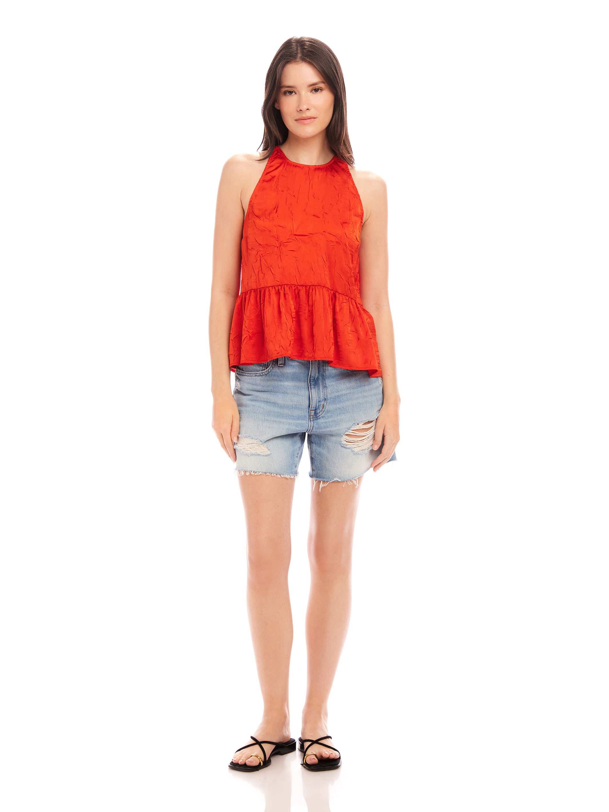 Woman wearing Floren ruffle hem halter top in red with distressed denim shorts and black sandals