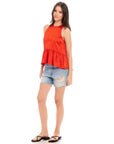 Woman wearing a sleeveless Floren Ruffle Hem halter top in orange crushed satin paired with ripped denim shorts and black sandals.
