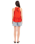 Woman wearing red Floren Ruffle Hem halter top with back tie and denim shorts, back view