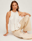 Woman wearing white Floren Ruffle Hem halter top with high-low hem and beige pants sitting on floor