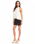 Woman wearing a sleeveless Floren Ruffle Hem Halter Top in white with black shorts and white heels.