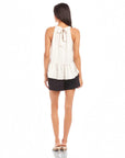 Back view of woman wearing Floren Ruffle Hem halter top with textured crushed satin and tie keyhole closure paired with black shorts