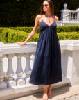 Woman wearing navy blue Leanna Midi Dress with adjustable spaghetti straps and V-neck standing outdoors by white balustrade