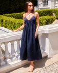Woman wearing a navy blue Leanna Midi Dress with adjustable spaghetti straps and V-neckline standing outdoors by a white railing