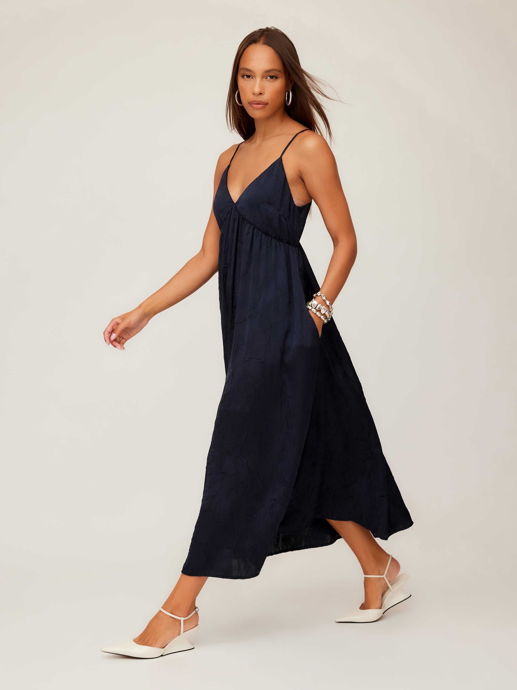 Woman wearing a black Leanna Midi Dress with crushed satin fabric, V-neckline, adjustable spaghetti straps, and flowing midi length.