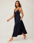 Woman wearing a black Leanna Midi Dress with crushed satin fabric, V-neckline, adjustable spaghetti straps, and flowing midi length.