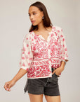 Woman wearing Rilyn Border Print Top with red watercolor border design and elbow blouson sleeves paired with black shorts