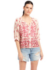 Woman wearing Rilyn Border Print Top with watercolor red floral design and elbow-length blouson sleeves paired with distressed denim shorts