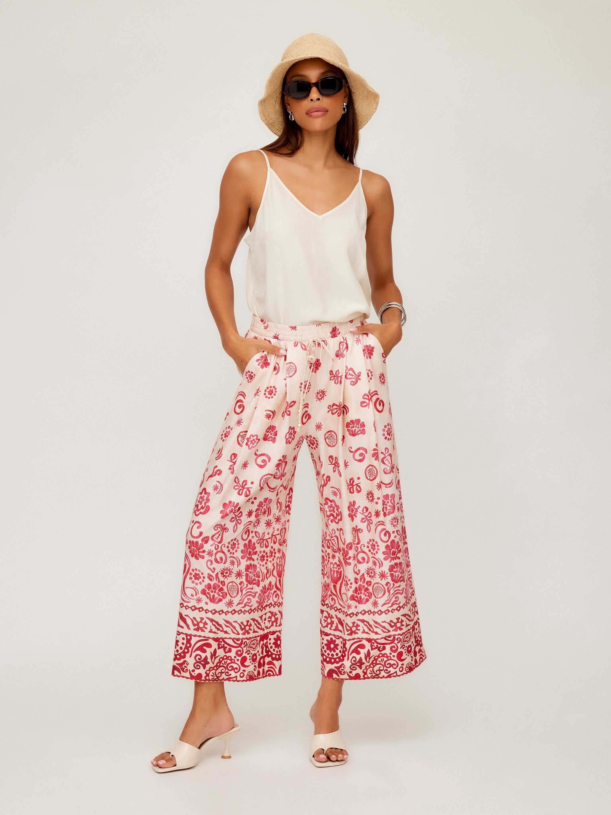 Woman wearing Etta Border Print Pants with wide leg and watercolor border design paired with a white sleeveless top and sunhat.