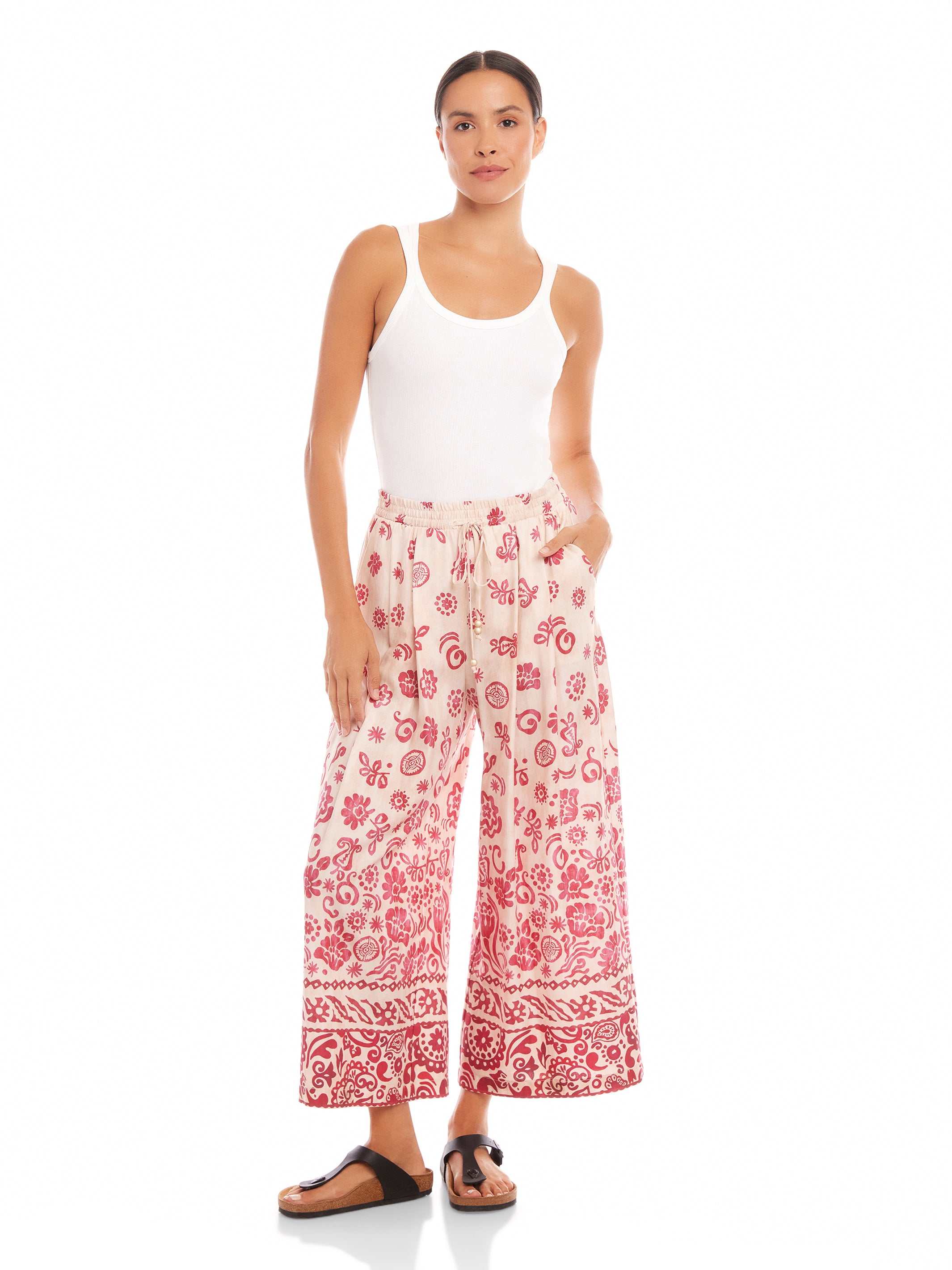 Woman wearing Etta Border Print Pants with wide leg, watercolor floral border design, elastic waistband, and side pockets.