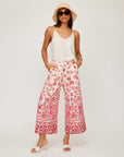 Woman wearing Etta Border Print Pants with wide leg and watercolor border design paired with a white sleeveless top and sunhat.