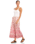 Woman wearing Etta Border Print Pants with wide leg and watercolor border print in red on cream, paired with white tank top and black sandals.