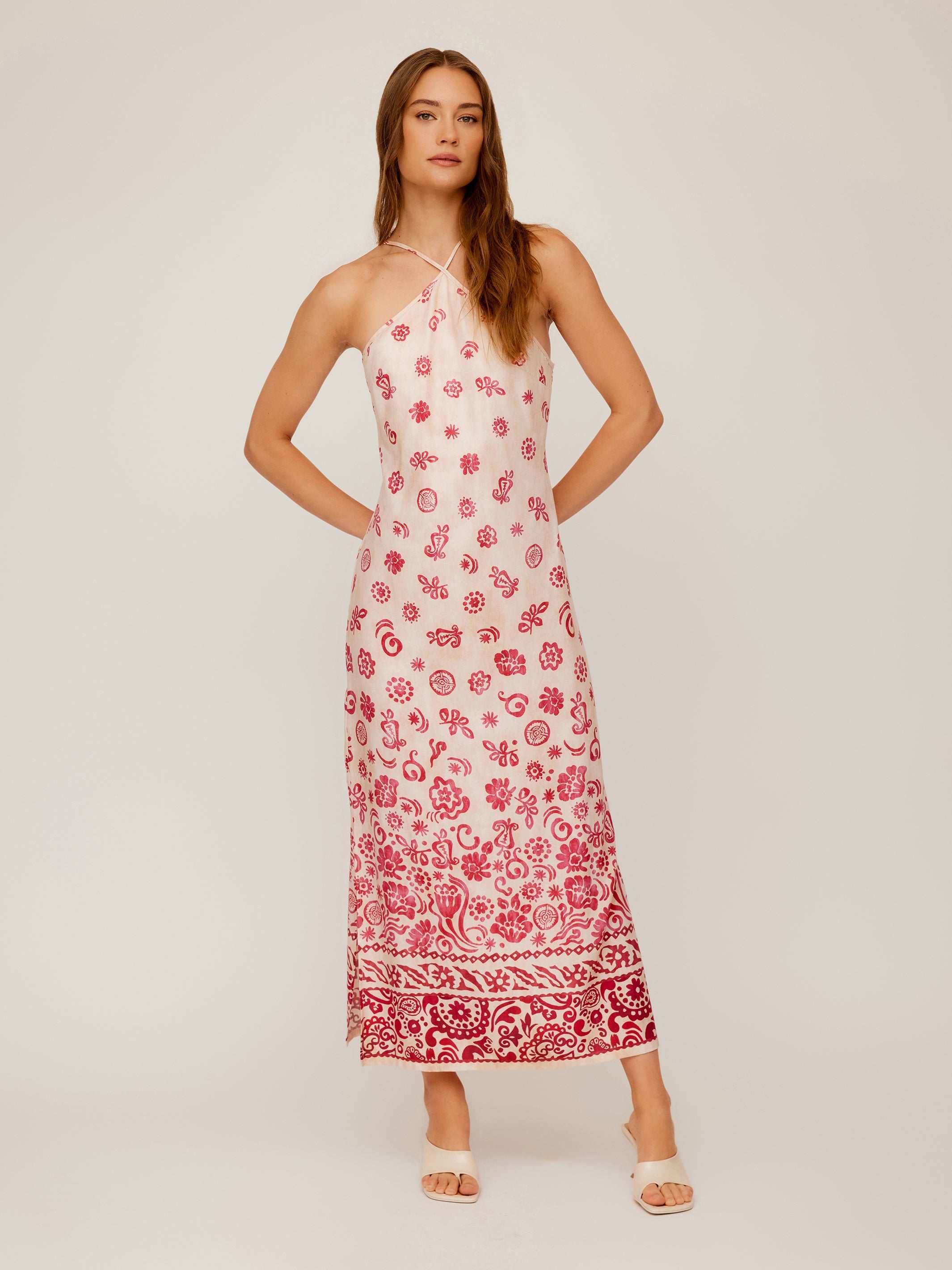 Woman wearing Jaylen Border Print Dress with pink floral watercolor border design, halter neckline, fitted silhouette, and side slits.