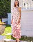 Model wearing a fitted Jaylen Border Print Dress with watercolor floral border design, halter neckline, and side slits, standing outdoors in sunlight.