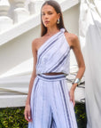 Woman wearing Vanita One-Shoulder Top in blue and white striped linen blend with matching high waist pants outdoors