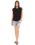 Woman wearing black Nora Fringe Tee with short fringe sleeves and side details paired with ripped denim shorts and black sandals
