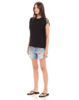 Woman wearing black Nora Fringe Tee with short fringe sleeves and blue ripped denim shorts