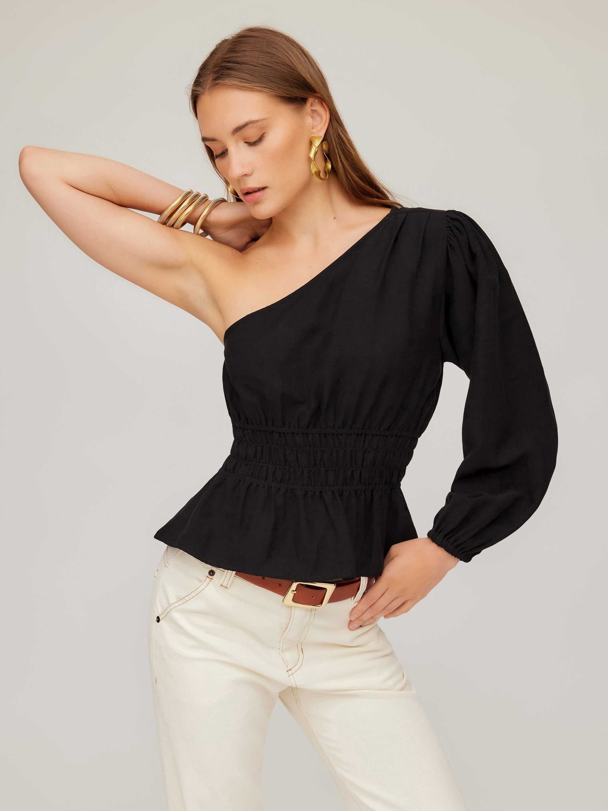 Woman wearing a black Talia One-Shoulder Top with elasticized waist and peplum hem paired with white pants