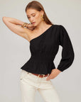 Woman wearing a black Talia One-Shoulder Top with elasticized waist and peplum hem paired with white pants